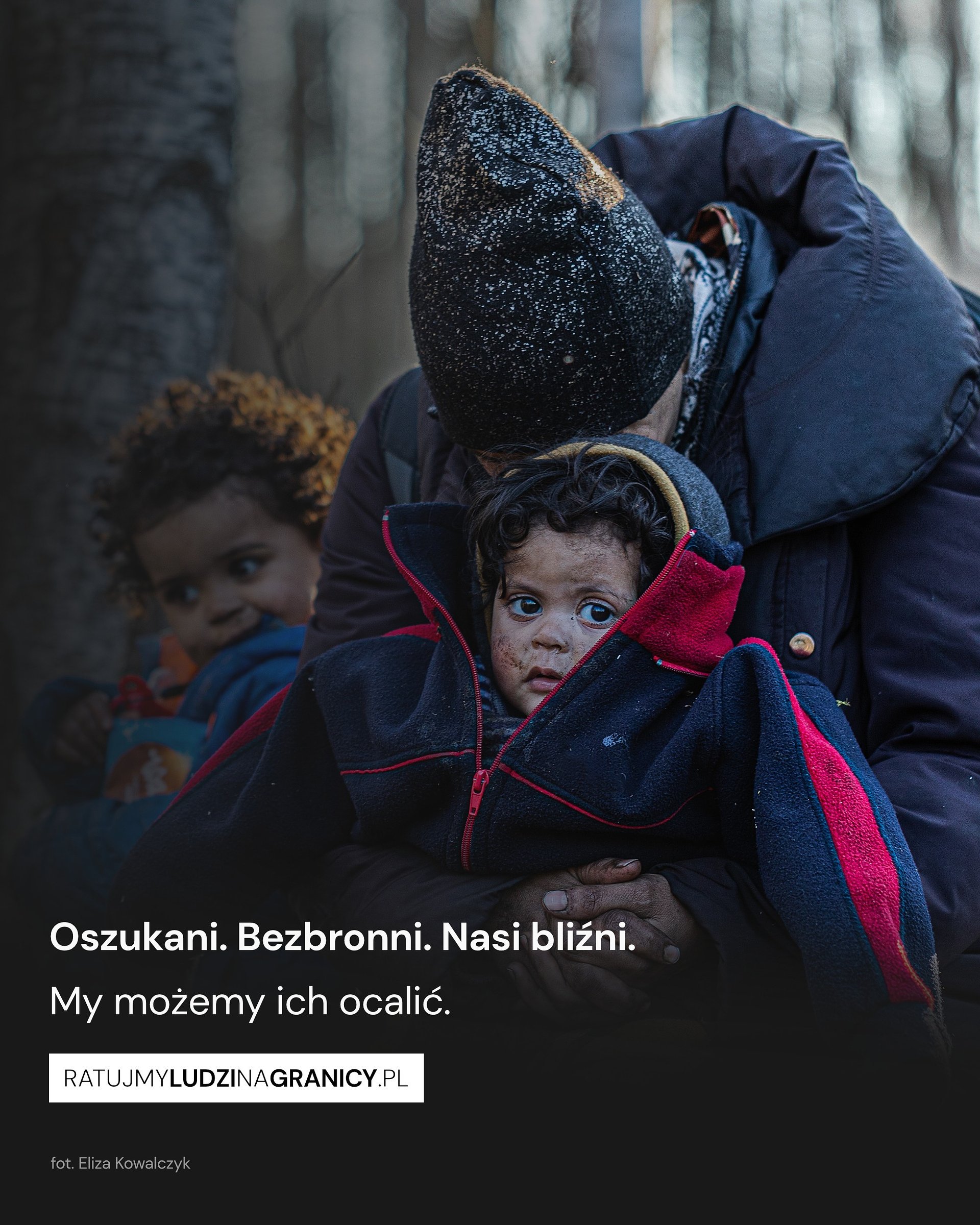 Zdjęcie przedstawia przedstawiające rodzinę migrantów w lesie. Na dole napis: Oszukani. Bezbroni. Nasi bliźni. My możemy ich ocalić. ratujmyludzinagranicy.pl. Autorką zdjęcia jest Eliza Kowalczyk.